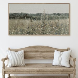 Puede incluir: Una pintura de paisaje enmarcada que representa un campo de flores silvestres en tonos de azul, blanco y verde. El fondo presenta una l&iacute;nea de &aacute;rboles en la distancia y un cielo nublado.