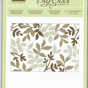 May include: A package for a Big Shot embossing folder featuring a layered leaves design. The leaves are in shades of brown and tan against a white background. The package includes text in English, French, and German.