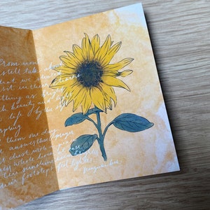 May include: A watercolour painting of a sunflower with a yellow centre and green leaves. The background is a light yellow watercolour wash. The text "Prom now still talk about what we shared dreams sit in their chairs as bright and beauty care life by the spring spring them one day prayer answers then a peace chest with at ease the whole love seem brighter the sunshine feel lighter. franziska beck." is written in white ink on the page.