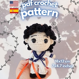 Puede incluir: Una muñeca de ganchillo con pelo negro rizado, grandes ojos negros y un traje de marinero blanco con cuello y corbata azules. La muñeca mide 18 por 12 cm. El texto dice pdf crochet pattern, @gawcreates e instant download.