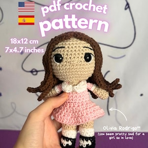 May include: A crochet doll with brown hair, a pink dress with a white collar, and black and white shoes. Text reads: pdf crochet pattern, 18x12 cm, 7x4.7 inches, Olivia Rodrigo!!! (you seem pretty sad for a girl so in love), instant download!