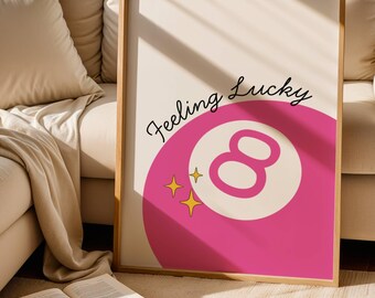 May include: A framed print featuring a pink eight ball with the number 8 in the center. The words "Feeling Lucky" are written above the eight ball in a cursive font. Two yellow stars are next to the eight ball.