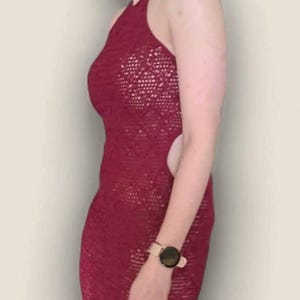 May include: A floor-length, deep red crochet dress featuring a halter neckline, open sides, and a detailed openwork knit pattern throughout the fabric. The garment is sleeveless and form-fitting, showcasing a consistent texture and color.