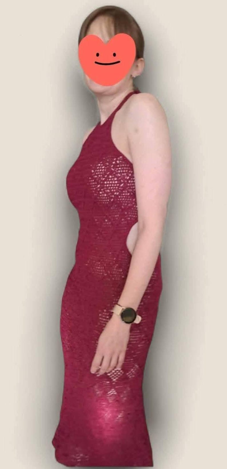 May include: A floor-length, deep red crochet dress featuring a halter neckline, open sides, and a detailed openwork knit pattern throughout the fabric. The garment is sleeveless and form-fitting, showcasing a consistent texture and color.