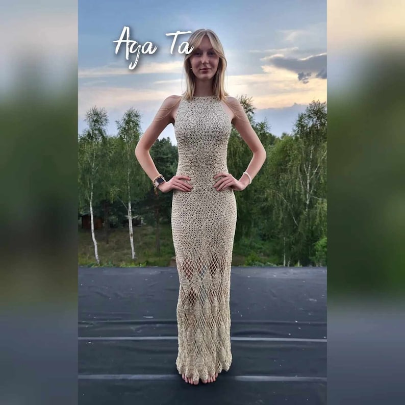 May include: A floor-length, beige crochet dress featuring a high neckline and a complex, open-work diamond pattern that transitions into a net-like structure toward the hem. The text "Aga Ta" is visible in white script at the top of the image.