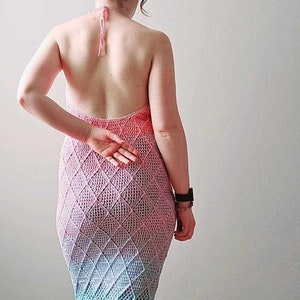 May include: A floor-length crochet dress featuring a halter neckline with tie straps and an open back. The garment displays a diamond-patterned stitch in a gradient color scheme transitioning from pink at the top to light blue at the hem. Craftelka Handmade.
