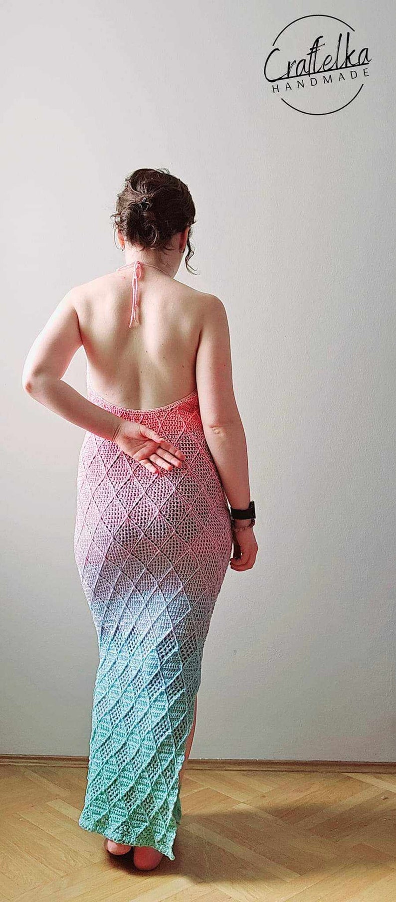 May include: A floor-length crochet dress featuring a halter neckline with tie straps and an open back. The garment displays a diamond-patterned stitch in a gradient color scheme transitioning from pink at the top to light blue at the hem. Craftelka Handmade.