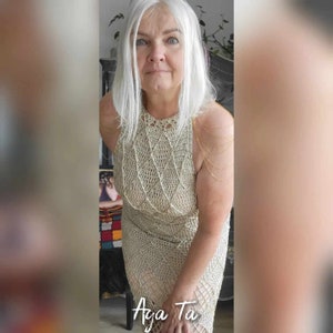 May include: A beige sleeveless crochet dress featuring a diamond-shaped pattern throughout the bodice and skirt. The garment has a high neckline and is accented with delicate gold-toned chain straps draped over the shoulders. The text Aga Ta is visible.