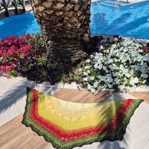 May include: A crescent-shaped crochet shawl featuring a gradient color pattern that transitions from a bright yellow center to bands of vibrant red and deep green, finished with a dark, scalloped lace edge along the entire curved perimeter.