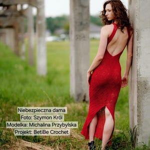 May include: A floor-length red crochet dress featuring a racerback design with a deep open back, a fitted bodice, and a central slit at the hem. The dress displays a textured, intricate pattern throughout the fabric, showcasing detailed craftsmanship.