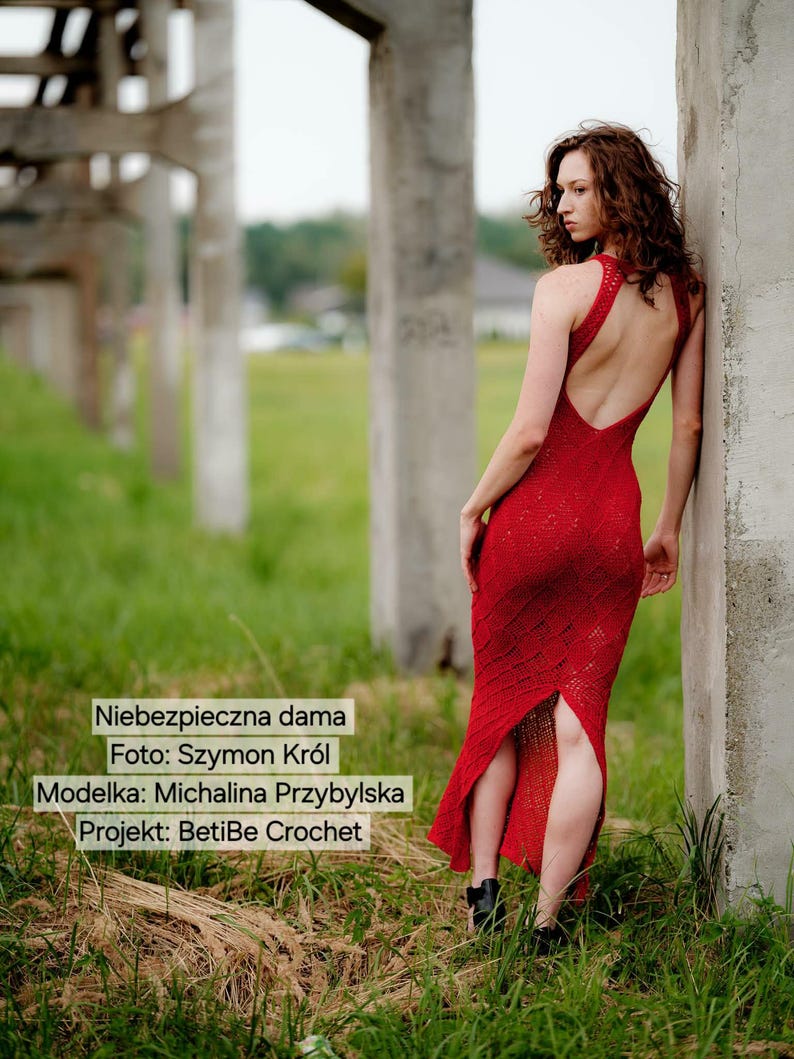 May include: A floor-length red crochet dress featuring a racerback design with a deep open back, a fitted bodice, and a central slit at the hem. The dress displays a textured, intricate pattern throughout the fabric, showcasing detailed craftsmanship.