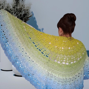 May include: A crocheted shawl with a gradient of blue, green, and yellow colors. The shawl is made with a delicate lace pattern and has a scalloped edge.