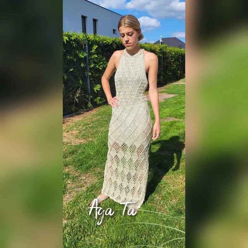 May include: A floor-length, sleeveless, cream-colored crochet dress featuring a repeating diamond pattern throughout the garment. The dress has a high neckline and a fitted silhouette that extends to the ankles. The text "Aga Ta" is visible at the bottom.