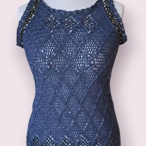 May include: A sleeveless blue crochet dress featuring a diamond pattern throughout the body. The garment is accented with dark metallic beads integrated into the neckline, armholes, and lower section, creating a textured and detailed appearance.