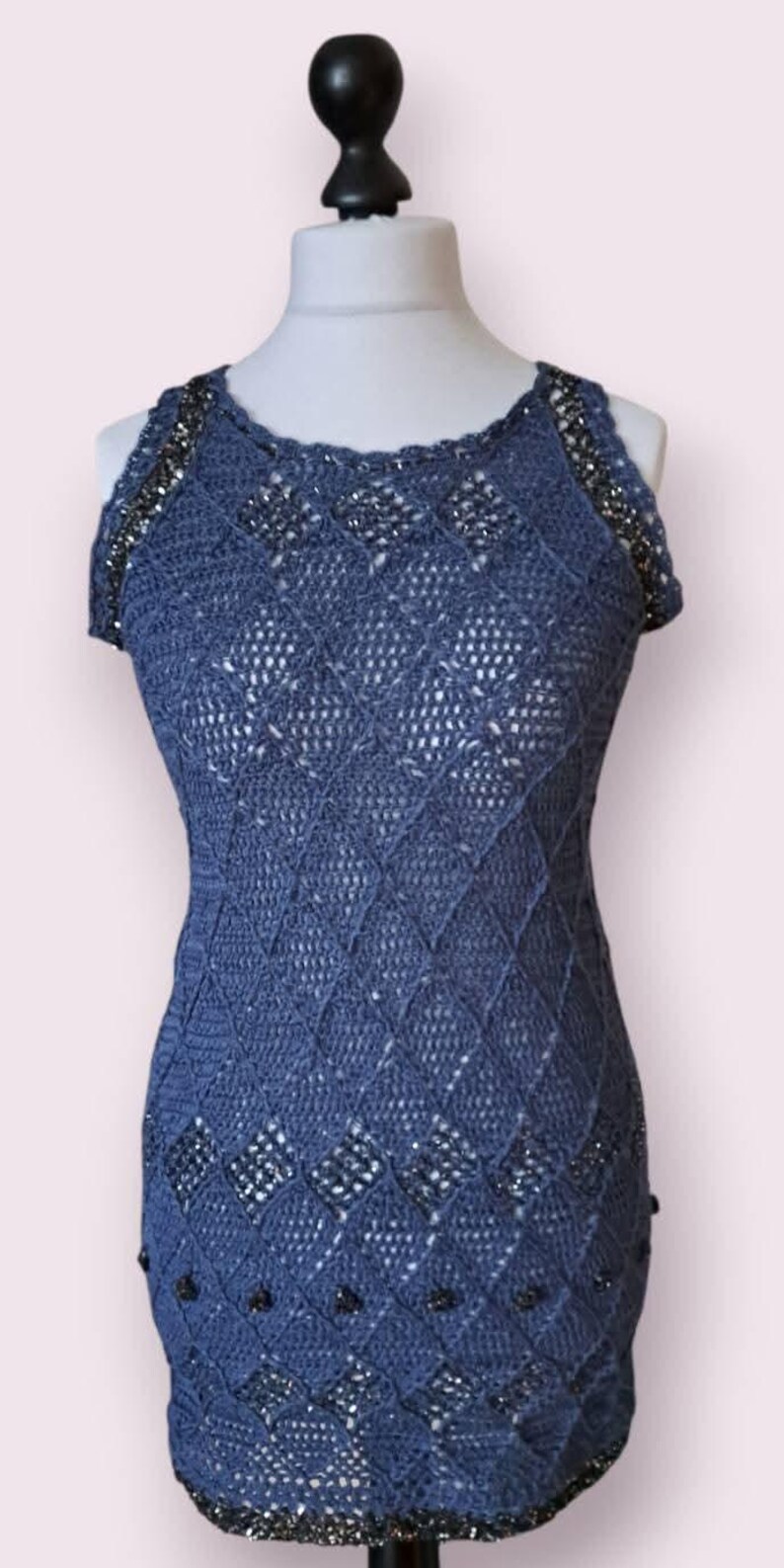 May include: A sleeveless blue crochet dress featuring a diamond pattern throughout the body. The garment is accented with dark metallic beads integrated into the neckline, armholes, and lower section, creating a textured and detailed appearance.