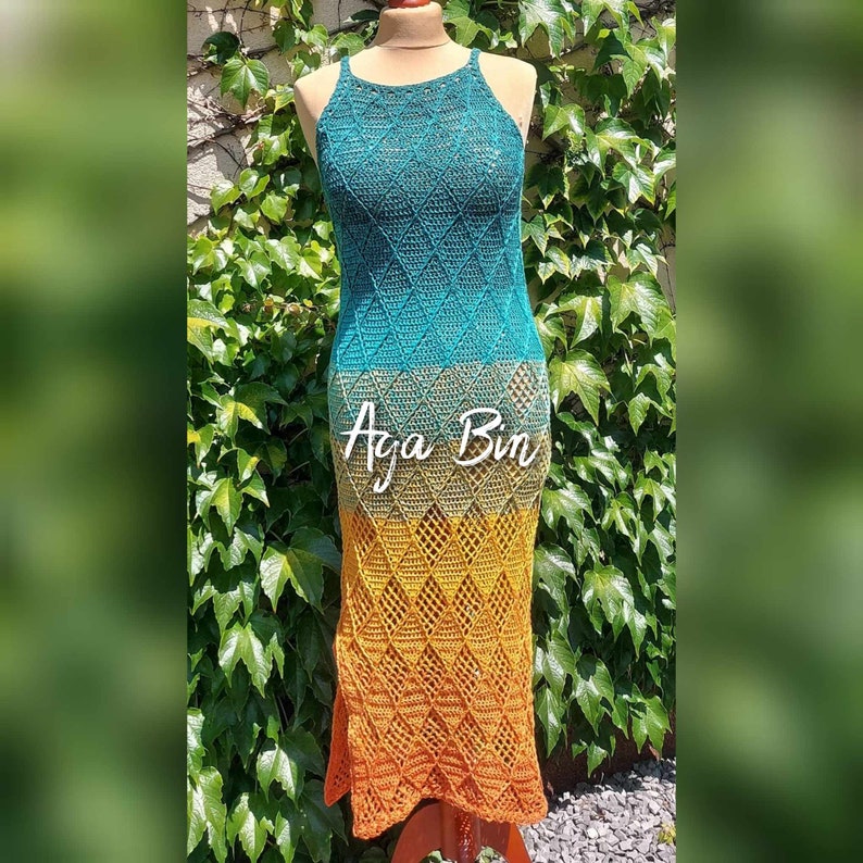 May include: A sleeveless crochet dress featuring a diamond pattern that transitions in color from teal at the top to olive green in the middle and orange at the bottom. The text Aga Bin is printed in white across the center of the garment.