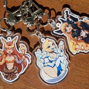 Può includere: Tre portachiavi in acrilico trasparente con illustrazioni di personaggi femminili dei cartoni animati. Ogni portachiavi ha un anello e un fermaglio in metallo argentato. I personaggi hanno i capelli lunghi e indossano abiti dorati, blu e neri.