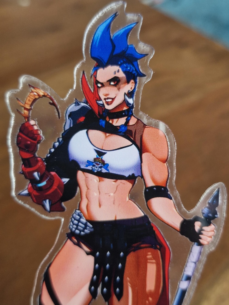 May include: A clear acrylic standee featuring a character with bright blue hair, wearing a white crop top with a skull emblem, black shorts, and red spiked arm armor. The character holds a curved golden blade in one hand and a spear in the other.
