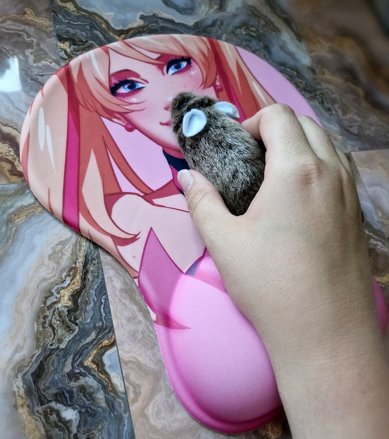 May include: A pink and white anime-style mousepad with a female character with long blonde hair. A small gray and brown plush mouse is on the mousepad.