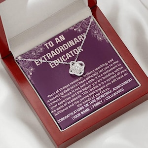 May include: A silver necklace with a knot pendant, presented in a red wooden box. The box contains a purple card with the text "TO AN EXTRAORDINARY EDUCATOR" and a message about achievement. A thoughtful gift.