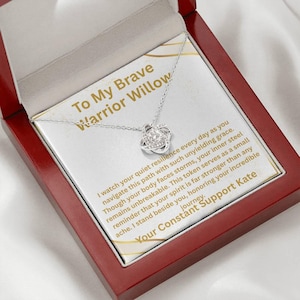 May include: A silver-colored necklace with a knot pendant, presented in a red wooden box. The box contains a card with text that reads "To My Brave Warrior Willow" and a supportive message. The necklace is a thoughtful gift.