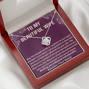 May include: A silver necklace with a knot pendant is displayed inside a red wooden gift box. The box contains a purple card with the text "TO MY BEAUTIFUL WIFE" and a message about faith and Ramadan.