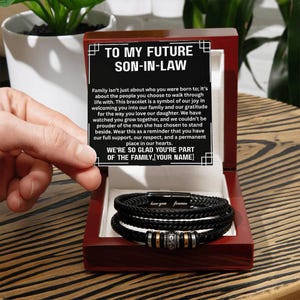 May include: A black braided leather bracelet with silver and gold accents, presented in a dark wooden box. The box contains a card with the text "TO MY FUTURE SON-IN-LAW" and a heartfelt message. The bracelet is inscribed with "love you forever".