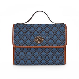 Puede incluir: Bolso de mano estampado en azul y marrón con asa superior y cierre de broche. El bolso presenta un diseño floral repetido y ribetes de cuero marrón. El asa es negra y el cierre es de color dorado.