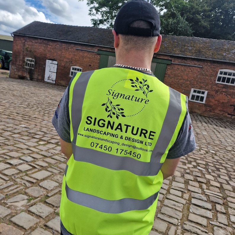 Puede incluir: Una persona lleva un chaleco de seguridad amarillo con el texto "SIGNATURE LANDSCAPING & DESIGN LTD" y el n&uacute;mero de tel&eacute;fono "07450 175450". El chaleco tambi&eacute;n tiene un logotipo con la palabra "Signature" en un c&iacute;rculo con un dise&ntilde;o de hojas.