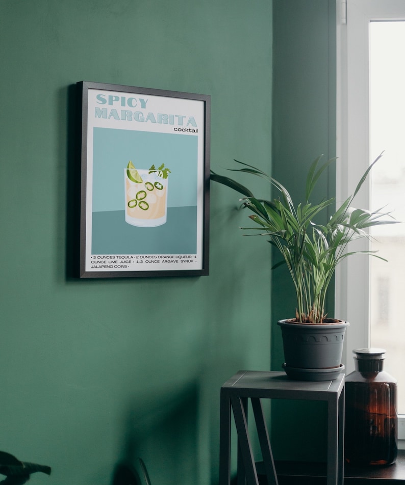 May include: A black framed poster with a white background and the text "Spicy Margarita cocktail" in a blue and green font. The poster features a glass of margarita with a lime wedge, cilantro, and jalapeno slices. The recipe is listed below the image.
