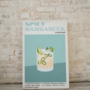 May include: A blue and white poster with the text "Spicy Margarita cocktail" and a drawing of a margarita cocktail with jalapeno slices in a glass. The recipe is listed below the image: "3 ounces tequila, 2 ounces orange liqueur, 1 ounce lime juice, 1/2 ounce agave syrup, jalapeno coins."