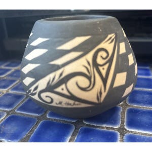 May include: Black and white pottery vase with a geometric design and a signature that reads "M. Haken".