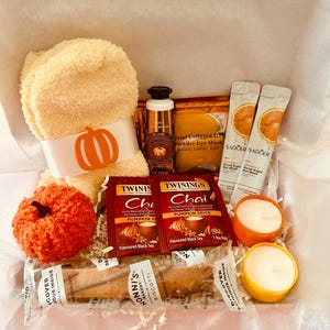 May include: A gift box filled with fall-themed items. Includes a plush orange towel with a pumpkin ribbon, a decorative orange pumpkin, Twinings Chai Pumpkin Spice tea, candles, eye masks, and biscotti.