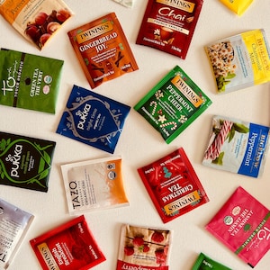 May include: Assortment of tea bags in various flavors, including English Breakfast, Peppermint Cheer, and Red Raspberry. The tea bags are in colorful packaging, with text labels. The image is taken from a top-down perspective.