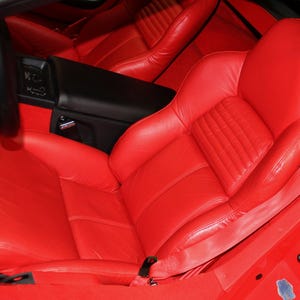 Può includere: Sedili auto in pelle rosso brillante con un pannello centrale trapuntato. L'interno presenta una console nera e cinture di sicurezza rosse. L'interno dell'auto è di un rosso vibrante.