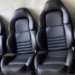 May include: Three black leather car seats with a blue, red, and white stripe design. The seats have a sporty look and are designed for comfort.