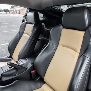 May include: The interior of a car featuring two black leather seats with tan inserts. The driver's seat is on the left and the passenger seat is on the right. The seats have headrests and are in good condition.