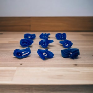 May include: A set of ten blue plastic cookie cutters in various shapes, arranged on a light brown wooden surface.