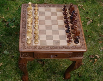 Peut inclure: Une table de jeu d'échecs en bois avec des sculptures complexes sur les côtés et les pieds. La table a un tiroir et un échiquier avec un jeu de pièces d'échecs.
