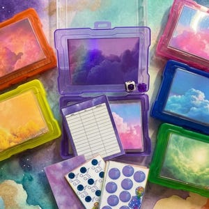 May include: An assortment of colorful, clear plastic cases with various inserts. The cases are in shades of purple, pink, blue, green, and orange. Some inserts feature cloud and sky imagery, while others have lined paper or patterned designs. Text at the bottom reads "Personalization of Categories optional."