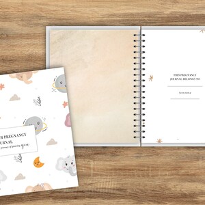 Puede incluir: Un diario de embarazo blanco con encuadernación en espiral. La portada presenta un patrón repetido de elefantes, estrellas, lunas y planetas. El texto en la portada dice "Our Pregnancy Journal. The journey of growing you."