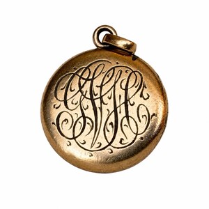 May include: A gold-colored, round pendant with an ornate, engraved monogram. The pendant has a loop at the top for a chain. The monogram is in a flowing, cursive style, adding a touch of vintage elegance. The pendant is isolated on a white background.
