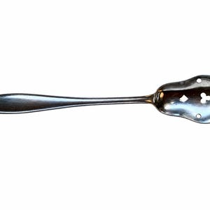 May include: A silver-colored slotted spoon with a decorative handle and a wide, perforated bowl. The bowl features a mix of round and clover-shaped cutouts. The handle has a floral design at the end.