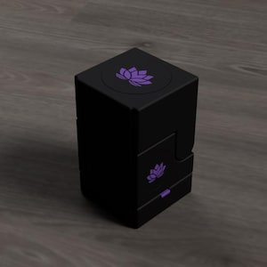 Könnte beinhalten: Eine schwarze, würfelförmige Box mit einem lila Lotusblumen-Design auf der Ober- und Vorderseite. Die Box hat eine Schublade und ein modernes Design. Die Lotusblume ist ein Symbol für Reinheit und Erleuchtung.