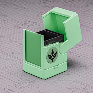Könnte beinhalten: Eine mintgrüne Box mit offenem Deckel, die ein schwarzes Innenfach freilegt. Auf der Vorderseite befindet sich ein kreisförmiges Emblem mit einem Blattdesign. Die Box steht auf einer grauen Oberfläche mit einem Bauplanmuster.
