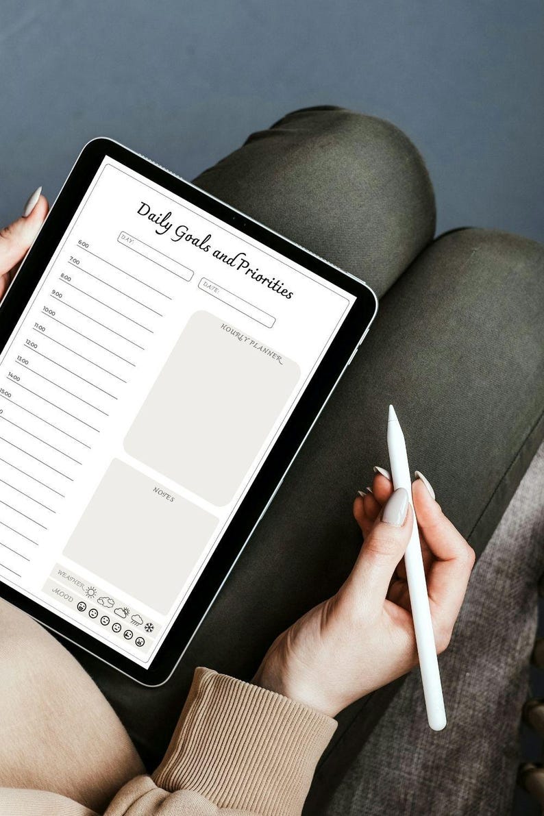 May include: A digital tablet displaying a daily goals and priorities planner with sections for hourly planning, notes, weather, and mood. The tablet is on a person's lap and a white stylus is being held in their hand.