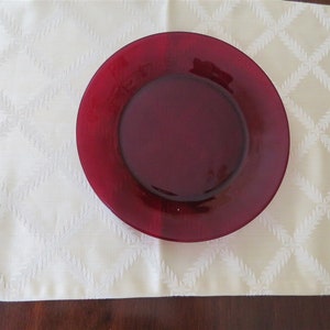 May include: A deep red glass dinner plate on a white table runner with a diamond pattern.