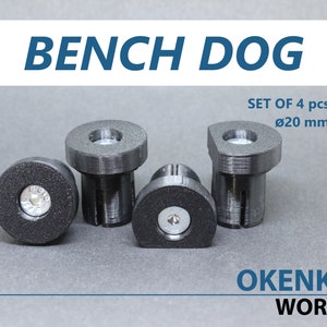 Può includere: Set di quattro piedini per mobili da banco in plastica nera, ognuno con un foro per vite e un diametro di 20 mm. Il testo "BENCH DOG" e "OKENKA WORKS" è visibile nell'immagine.