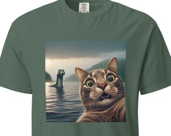 May include: A green t-shirt with a graphic of a cat taking a selfie with the Loch Ness Monster in the background.