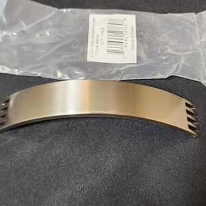 May include: A brushed nickel drawer pull with a curved shape and five vertical lines on each side. The pull is packaged in a clear plastic bag with a label that reads "2 1/4" ZINC DRAWER PULL, CODE #101M, QTY 1 PIECE, MADE IN CHINA."